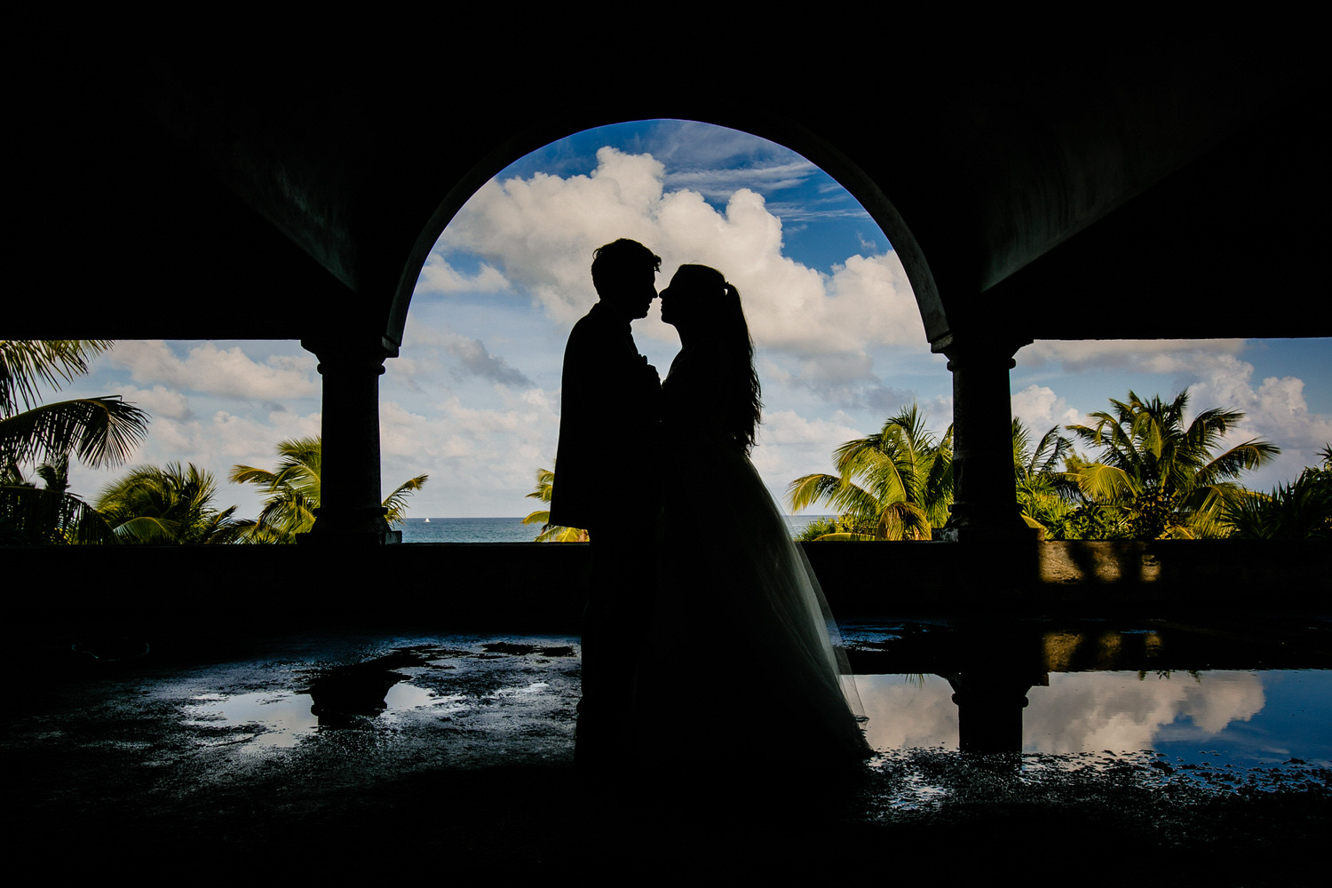 Silueta de una pareja recién casada bajo un arco frente al mar