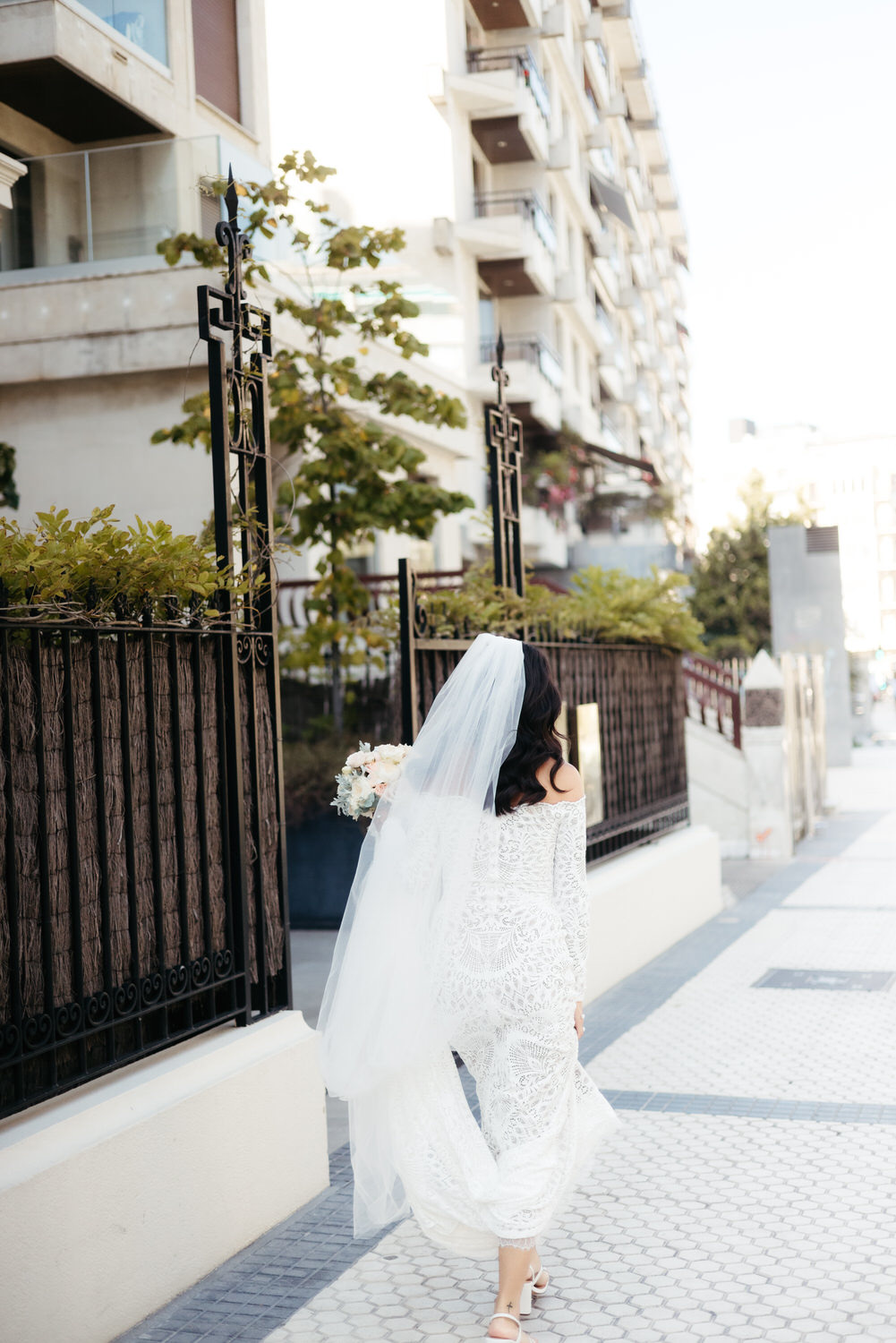 Novia caminando por una calle urbana con velo y ramo