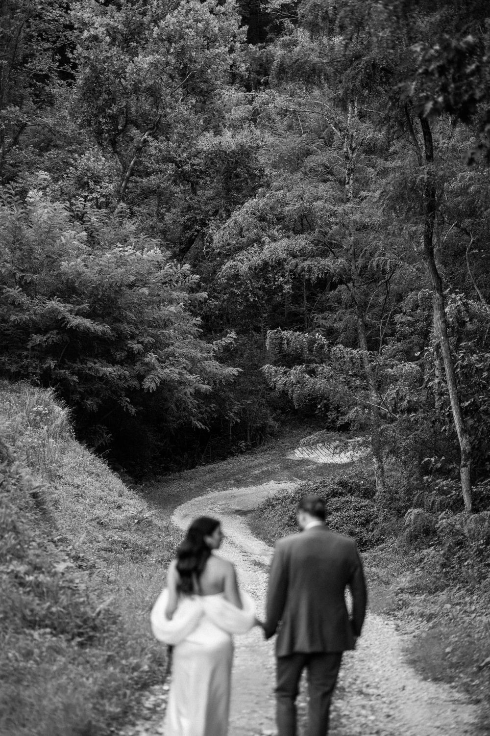 Pareja caminando de la mano por un sendero en el bosque, en blanco y negro